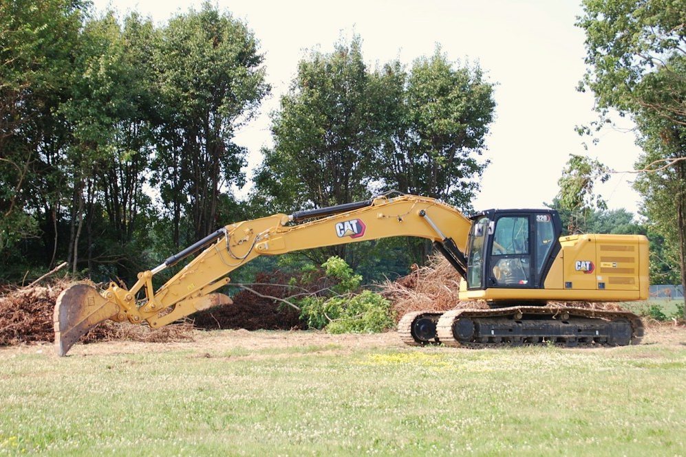An excavator clearing small trees and stumps from a wooded lot
